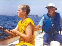 Photo by Meredith J. Rushing Conrad at the helm with Alex fishing on the trip out to Damariscove Island. The beautiful sunshine would soon give way to much rougher weather.