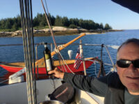 Capt. Dan prepares to celebrate after anchoring at Merchants Row. Inset, the author on Isle au Haut with Bailamos in the background.Photos courtesy Jacqueline Llewellyn
