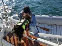 Photos by Marilyn Pond BrighamAbove, the ancient and aptly named Still Afloat with a rubrail that serves to cushion blows from other boats, and also hides some repair work. At right, Paul helps the couple’s dog into the newer of their dinghies, an inflatable named Quellefois.