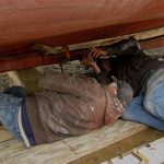 Now that a clamp has tightened the plank in more, Jimmy puts in a couple more screws.